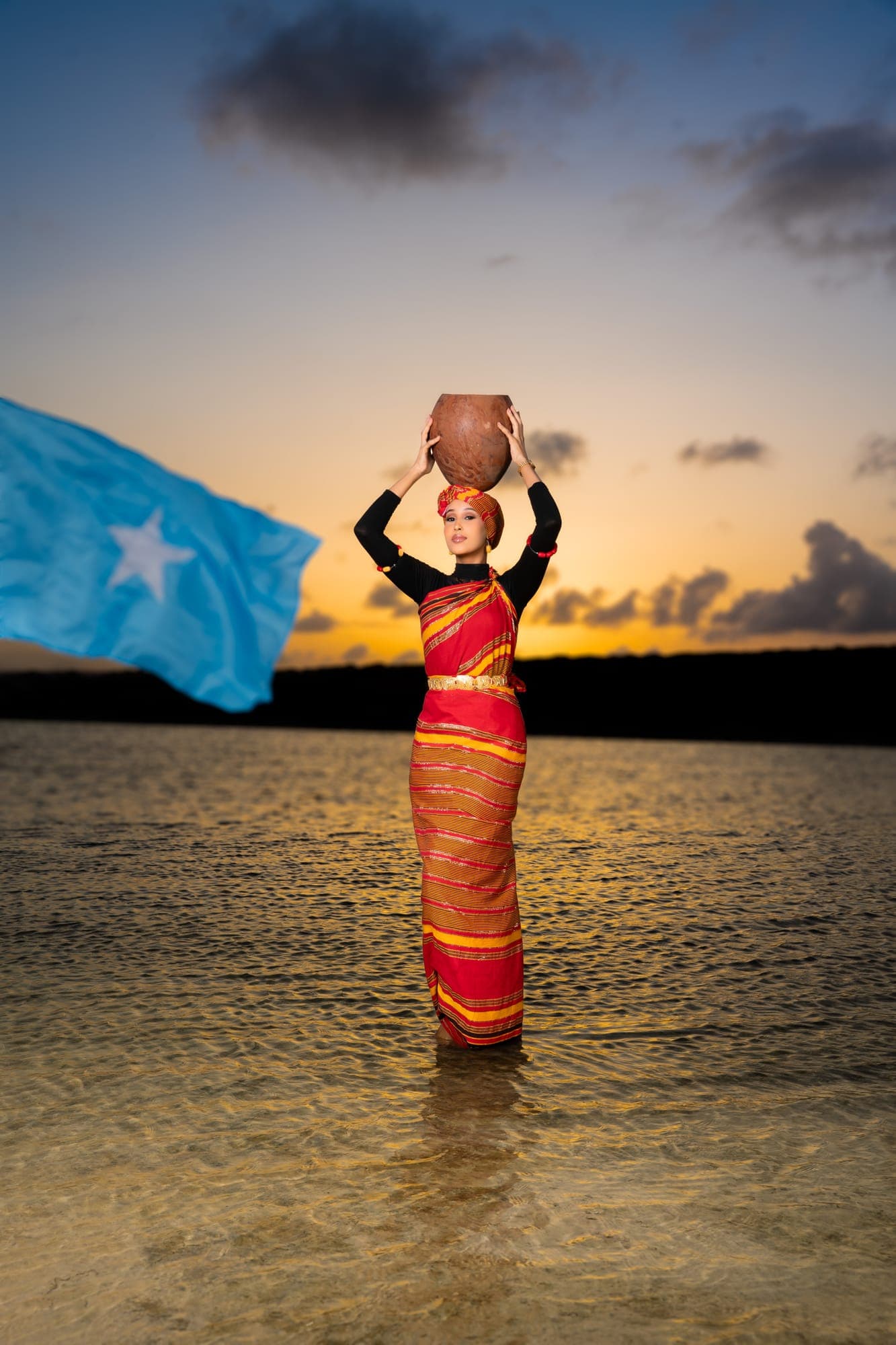 Haweeney Soomaaliyeed oo xiran guntiino casaan iyo dahab ah, madaxana ku sidata dheri biyood, qorrax-dhac agtiisa calanka Soomaaliyeed